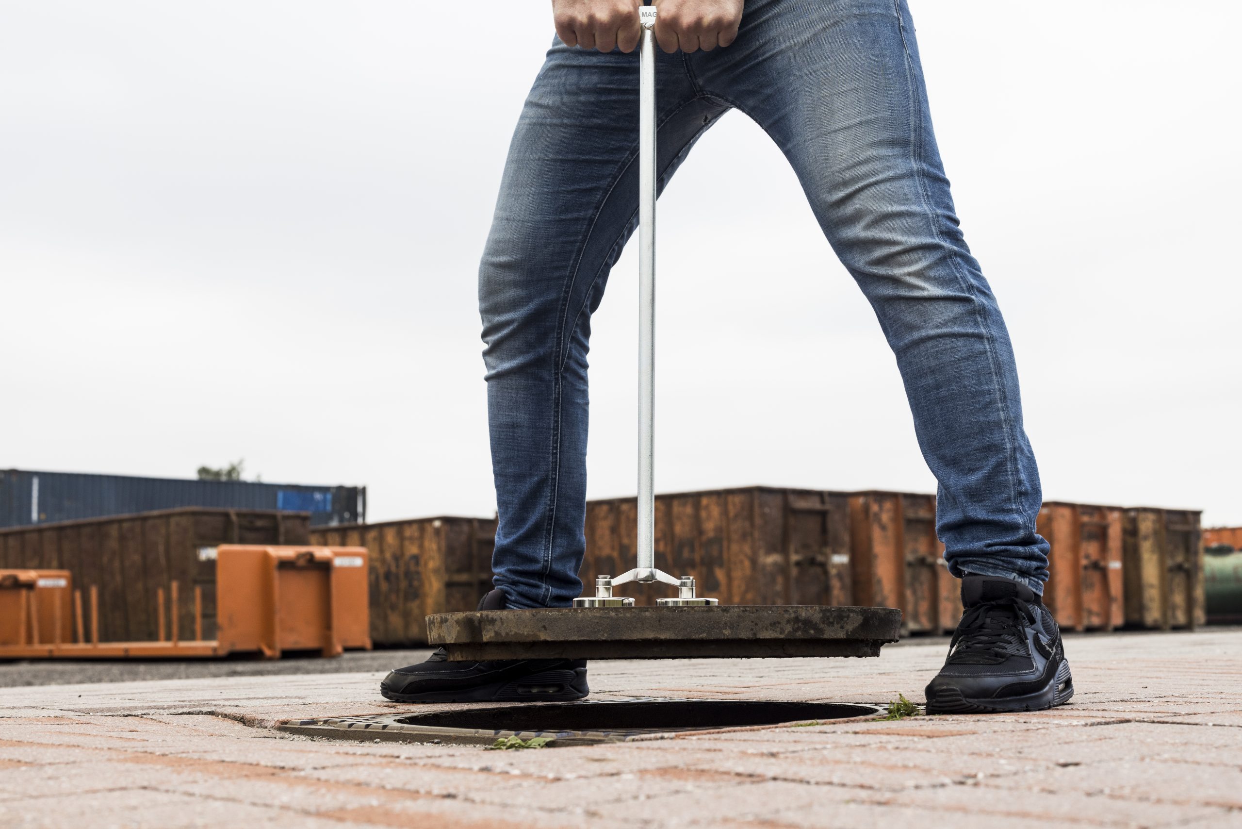 Man heft zware putdeksel met lange stang en industriële magneet, ideaal voor gemeentewerk en professioneel gebruik.
