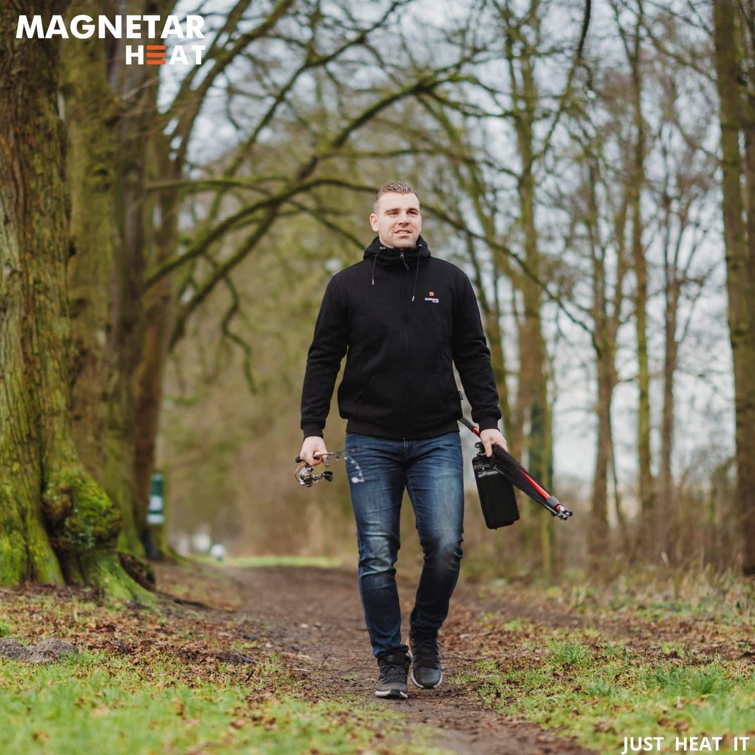 Glimlachende man met een zwarte verwarmde vest loopt buiten in het bos met visspullen, hij voelt zich comfortabel vanwege de verwarming