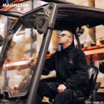 Man met zwarte verwarmde jas zit op een heftruck en kijkt omhoog, genietend van de verwarming in de jas