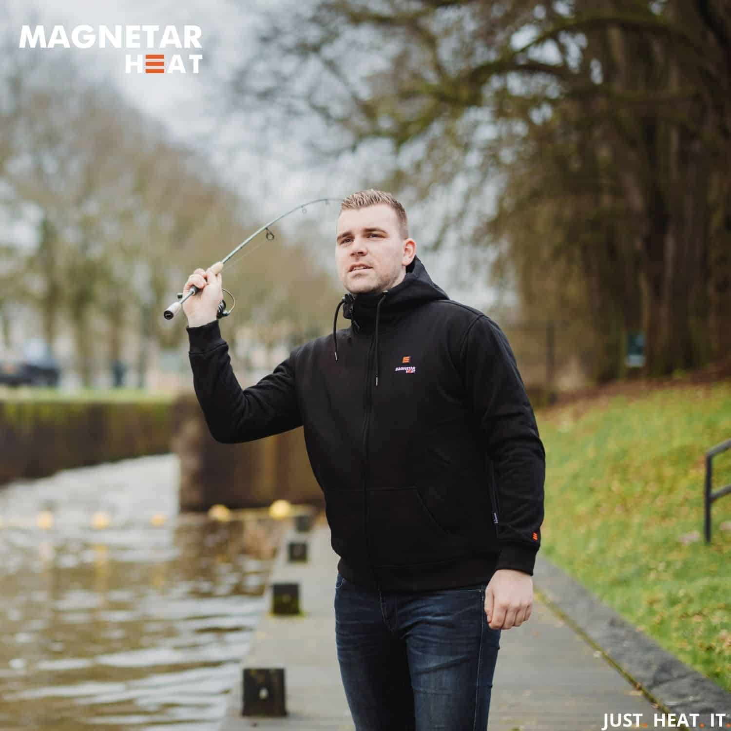 Mannelijke visser gooit zijn hengel uit in het water terwijl hij geniet van de zwarte verwarmde vest met rits die aan staat