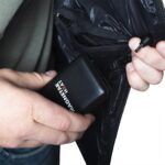 Magnetar Heat powerbank met aansluitkabel in binnenzak van jas, essentieel voor het voeden van verwarmde kleding.